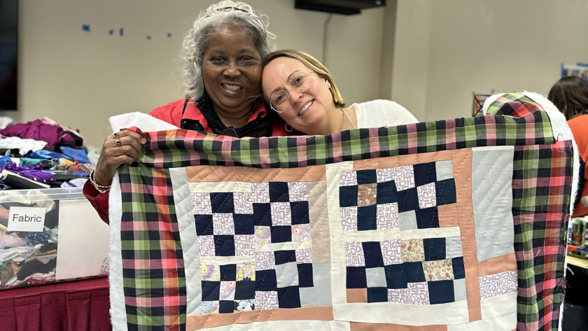 image of two women smiling and holding up a colorful patchwork quilt at Gee's Bend